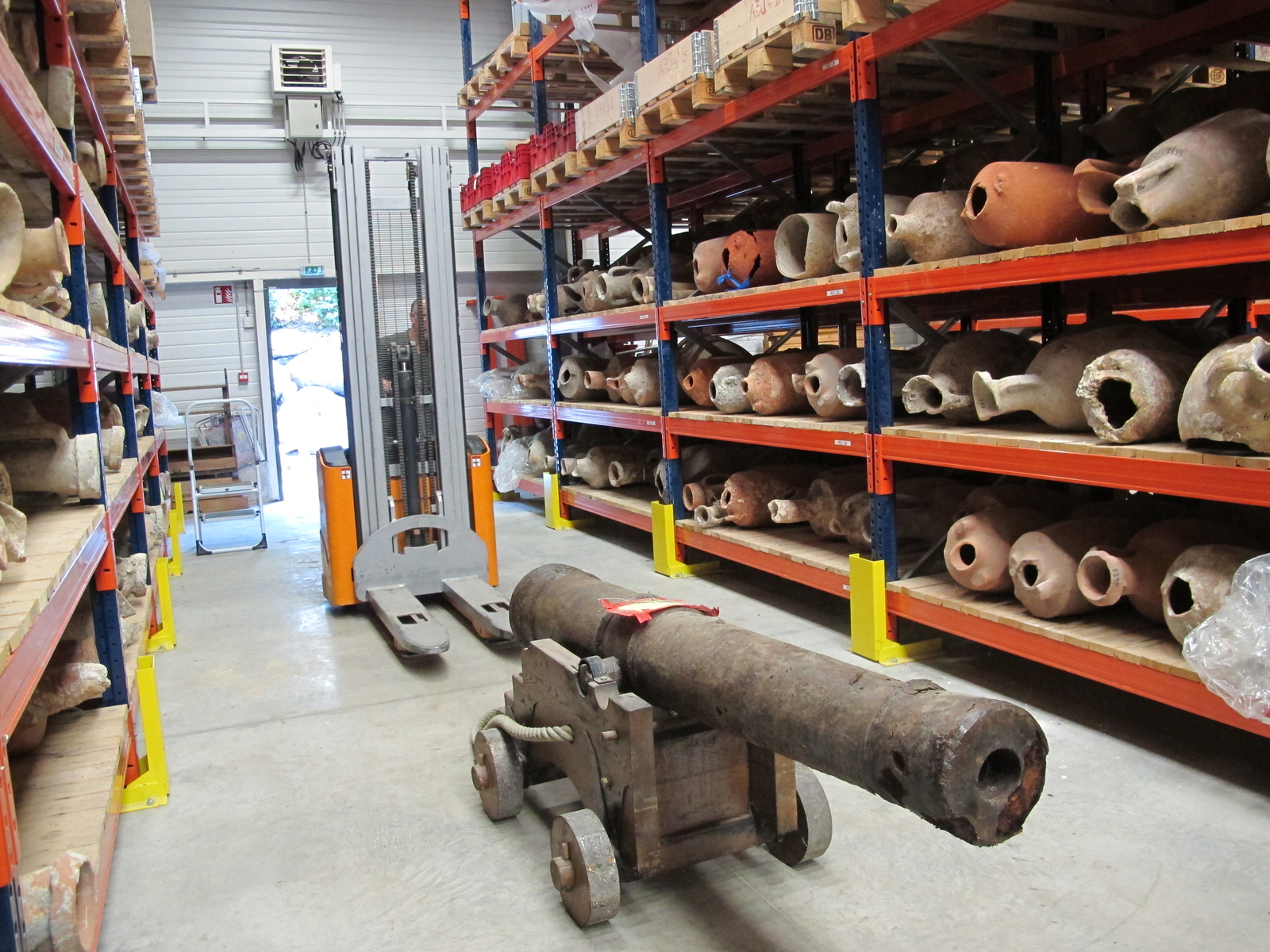 Photographie des locaux intérieurs du DRASSM avec des étagères remplies d'amphores et un canon