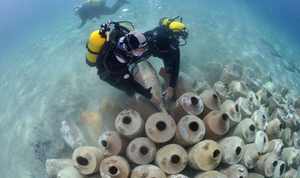Photographie d'un plongeur sous l'eau au-dessus d'amphores