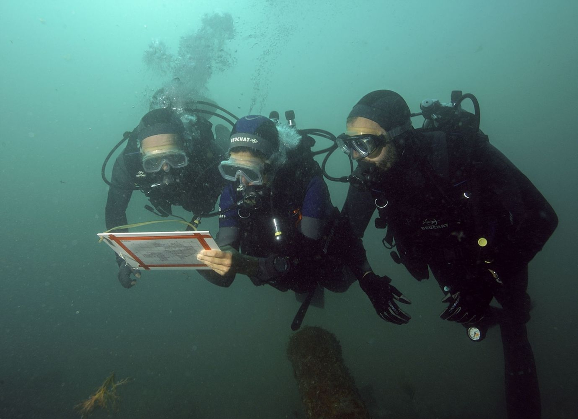Photographie sous-marine de trois plongeurs effectuant un relevé
